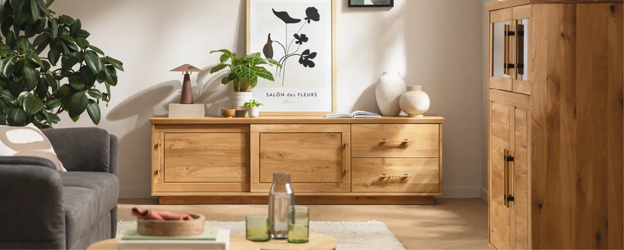 Wohnzimmer mit Sideboard und Vitrine aus Massivholz im natürlichen Design. Hochwertige Wohnzimmermöbel mit Holzmaserung, kombiniert mit Pflanzen, Dekoration und Sofa für stilvolles Wohnen und nachhaltige Einrichtung.
